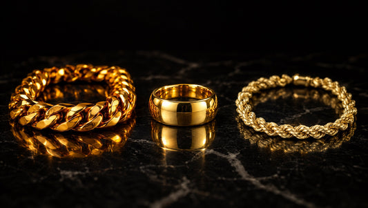Gold Cuban link chain, gold band ring, and gold rope chain on black marble showing the color difference between 24K, 18K, and 14K gold